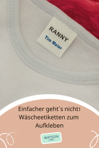 Waescheetiketten-zum-Aufkleben-in-Kleidung-mit-Namen-von. Das kleine weisse Etikett im Format 23 x 6 mm aus weisser Folie mit blauer Schrift klebt auf dem Wäsche Etikett des weißen T-Shirts